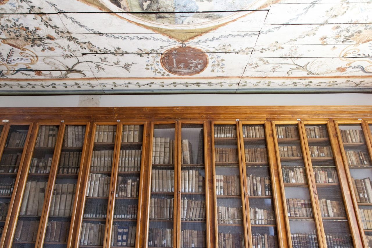 Le scaffalature di libri antichi sotto il soffitto ligneo dipinto delle Biblioteche Riunite di Agnone